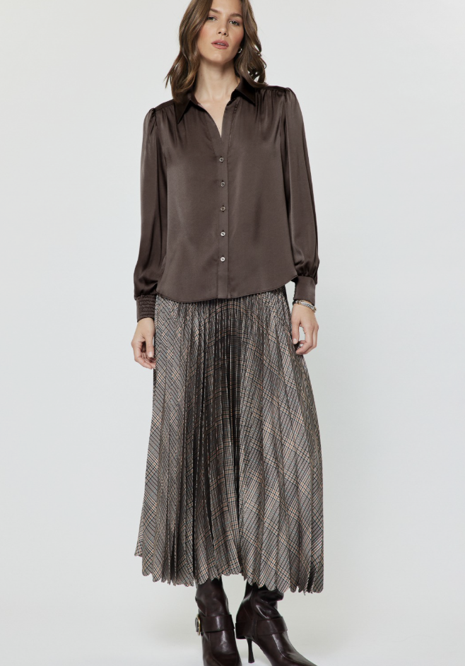 A woman modeling a Current Air gray and brown plaid pleated midi skirt and dark brown heeled ankle boots, set against a plain light gray studio background.