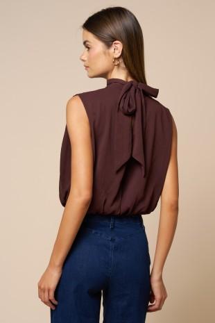 Woman wearing a brown sleeveless top with a bow detail on a beige background