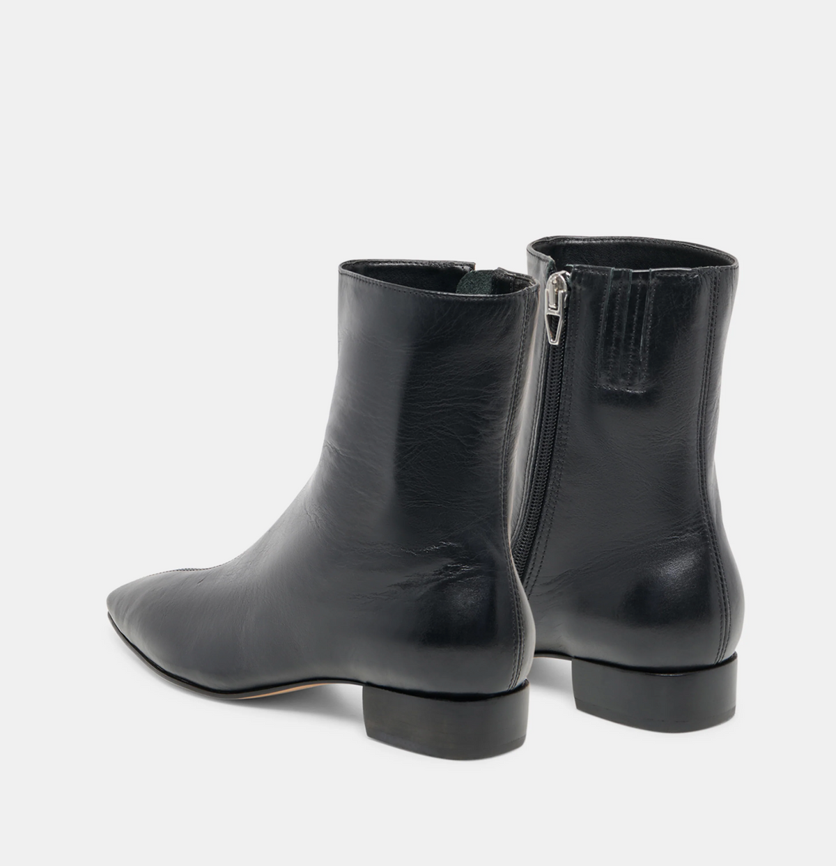 A pair of Dolce Vita Tarine black leather ankle boots with a pointed toe and side zipper, shown from the rear three-quarter view on a light gray background.