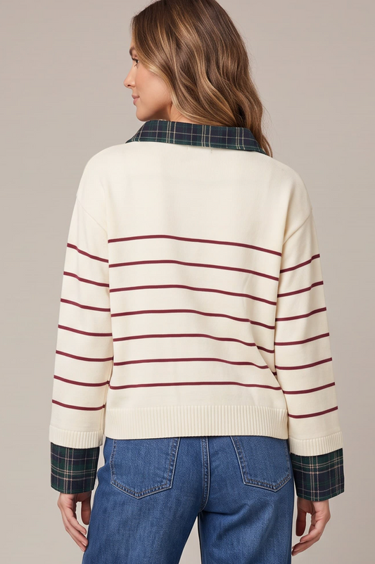 A woman shown from the back wearing a cream knit sweater with thin burgundy horizontal stripes, a dark green plaid collar, and matching plaid cuffs, paired with blue jeans against a solid beige studio background.
