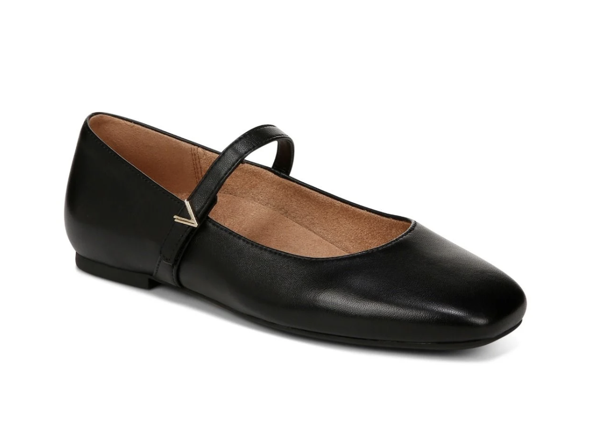 A black leather Vionic Alameda Mary Jane flat shoe with a rounded toe and a small gold chevron accent on the strap, shown on a white background.