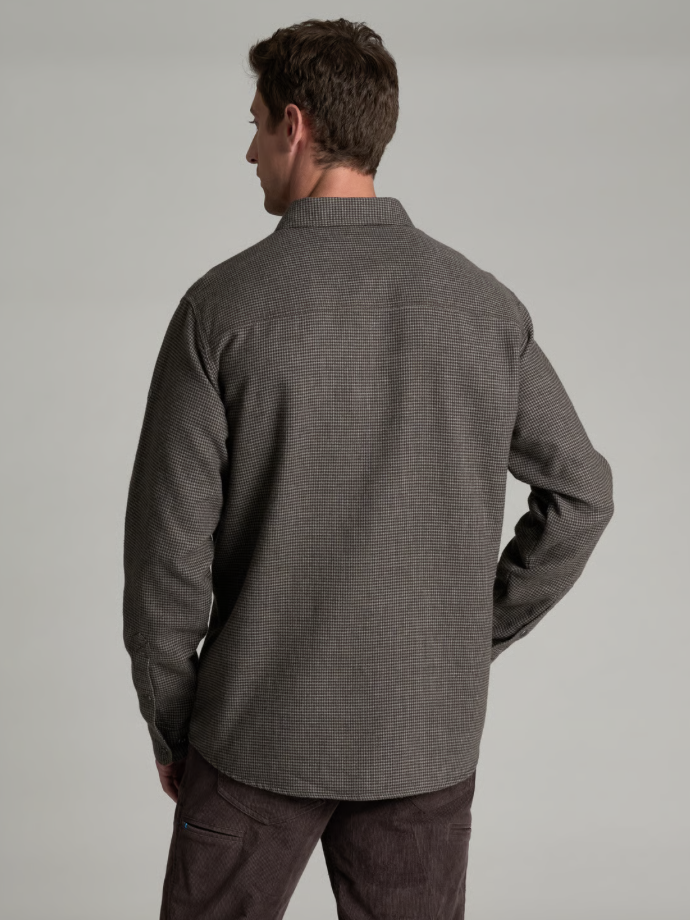 A man viewed from the back wearing a dark gray textured long-sleeve button-up KÜHL Disputr shirt and brown corduroy pants, set against a plain light gray studio background.