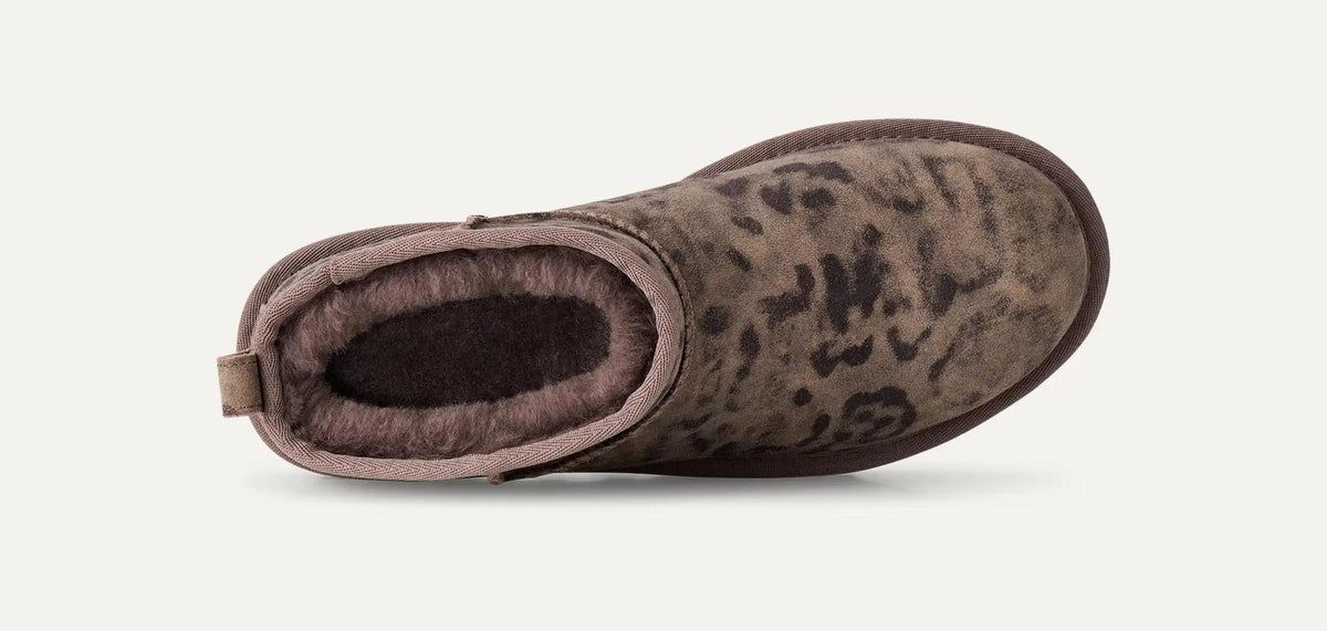 A single Classic Ultra Mini ankle-height boot with a brown and beige leopard print upper and a dark brown plush lining, shown from a side profile on a light off-white background.