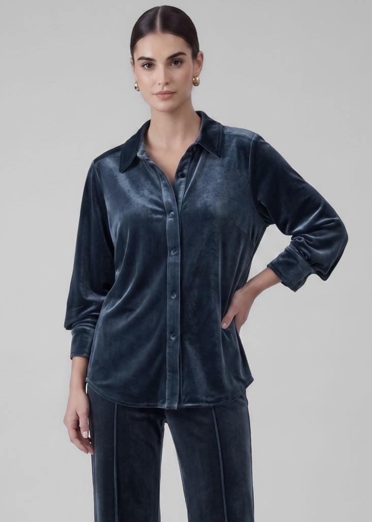 A woman modeling a dark navy blue velvet button-up shirt and matching velvet trousers against a solid light gray studio background.