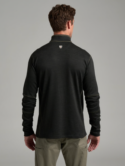 A man viewed from the back wearing a  Kuhl Ryzer dark charcoal gray long-sleeve quarter-zip pullover with a small shield logo on the upper neck, paired with khaki pants, against a solid gray studio background.