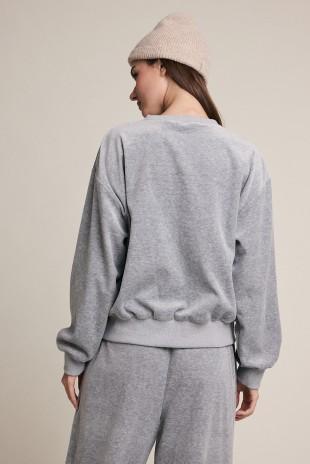 A woman shown from the back wearing a light gray heather Raisonnel crewneck sweatshirt and matching sweatpants, paired with a beige knit beanie, against a solid light beige background.