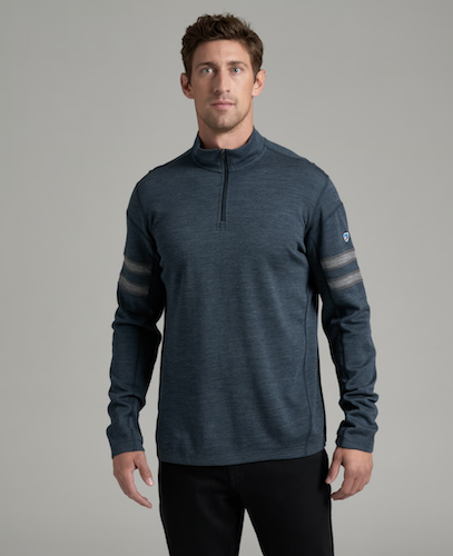 A man wearing a Kuhl Team dark slate blue heathered quarter-zip pullover with gray striped details on the sleeves, paired with black pants, against a solid gray studio background.