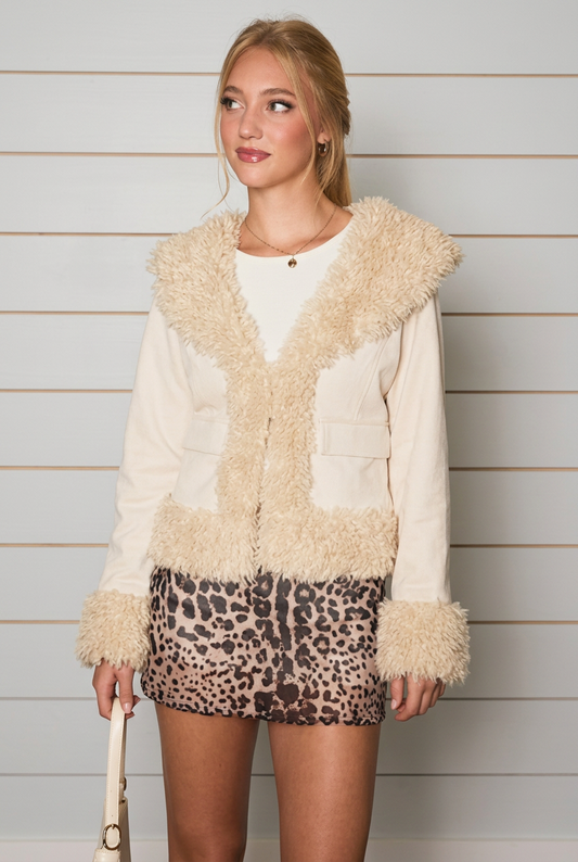 A woman modeling a cream faux-fur trimmed jacket with a leopard-print mini skirt, standing against a solid light gray background.