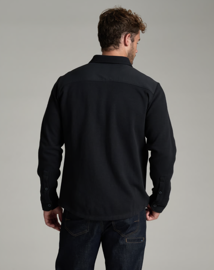 A man viewed from the back wearing a black Kuhl TRelentr standing against a neutral gray studio background.