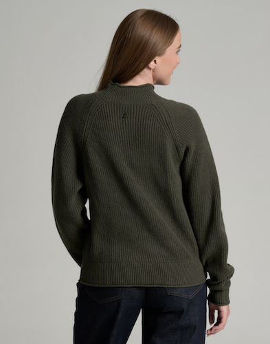 A woman viewed from the back wearing an olive green Kuhl Strova ribbed knit sweater and dark jeans against a plain light gray studio background.