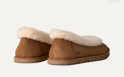 A pair of UGG slip-on ballet flats in tan suede with a thick cream shearling lining, shown from the back on a light off-white background.