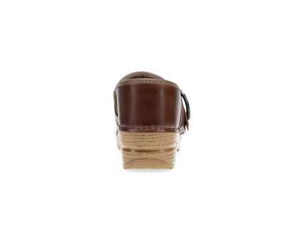 A single brown leather Dansko clog shoe shown from the back, featuring a stacked tan and brown platform sole with a small buckle detail on the side, set against a plain white background.
