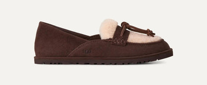 A dark brown suede UGG Zora slip-on loafer with a light beige shearling lining and a matching brown leather tassel detail, shown against a plain off-white background.