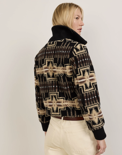 A woman shown from the back wearing a cropped knit sweater with a black base and a beige and brown Southwestern-style geometric pattern, paired with cream pants, against a plain light gray studio background.