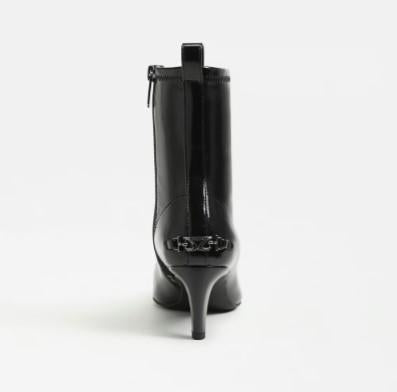 A Circus Inez black patent leather ankle boot with a kitten heel and a decorative chain detail on the back of the heel, shown from a rear three-quarter view against a plain white background.