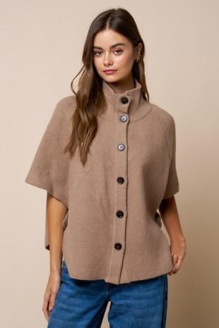 Woman wearing a taupe poncho with button details against a beige background