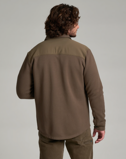 A man viewed from the back wearing a brown Kuhl Relentr long-sleeve fleece pullover with a slightly lighter olive-brown yoke across the shoulders, paired with brown pants, against a solid light gray studio background.