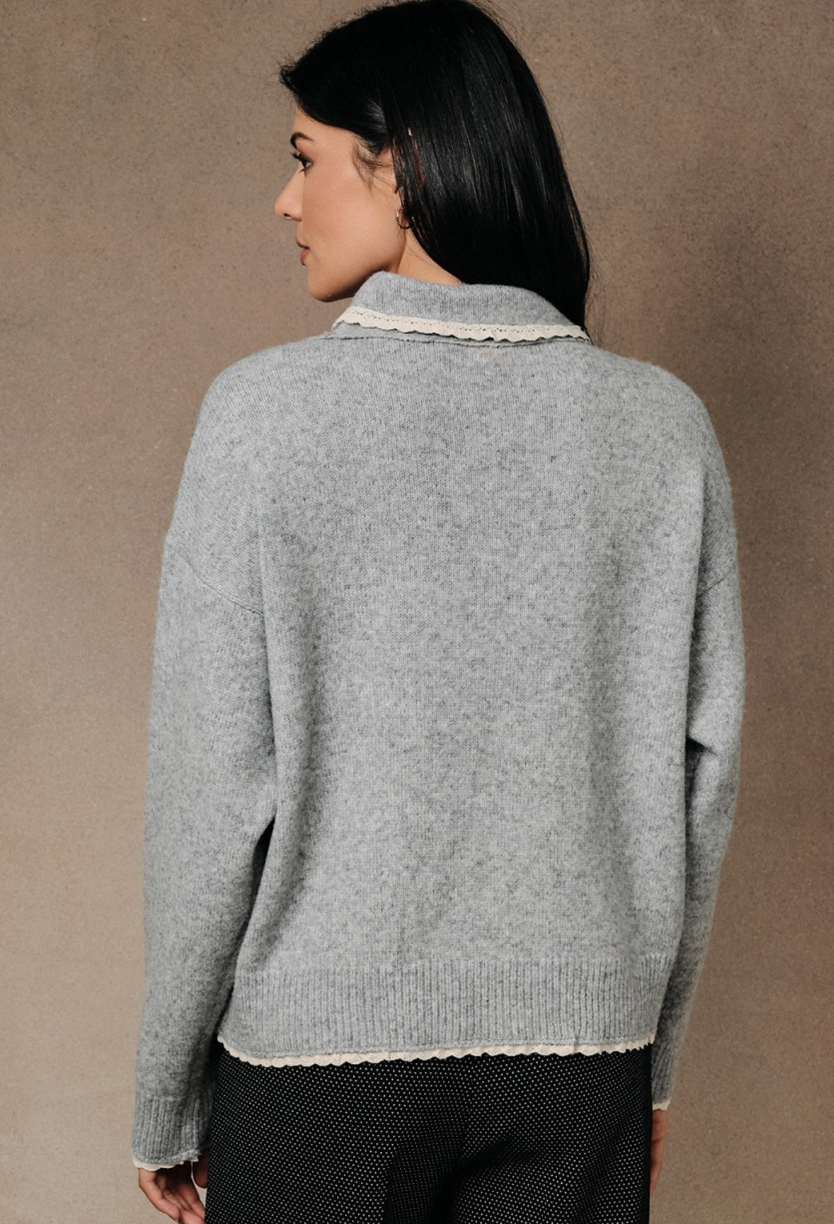 A woman shown from the back wearing a Heather gray scarf‑neck sweater with relaxed silhouette and soft brushed knit, paired with black textured pants, against a neutral textured studio backdrop.