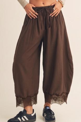 Brown wide-leg pants with lace trim worn by a person on a beige background