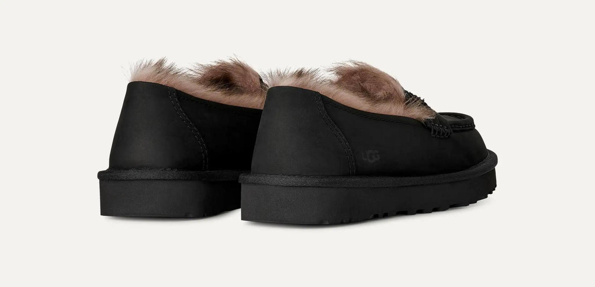 A pair of UGG Ellis Nubuck black slip-on slippers with tan shearling-style lining visible at the top, shown from the back on a light off-white background.