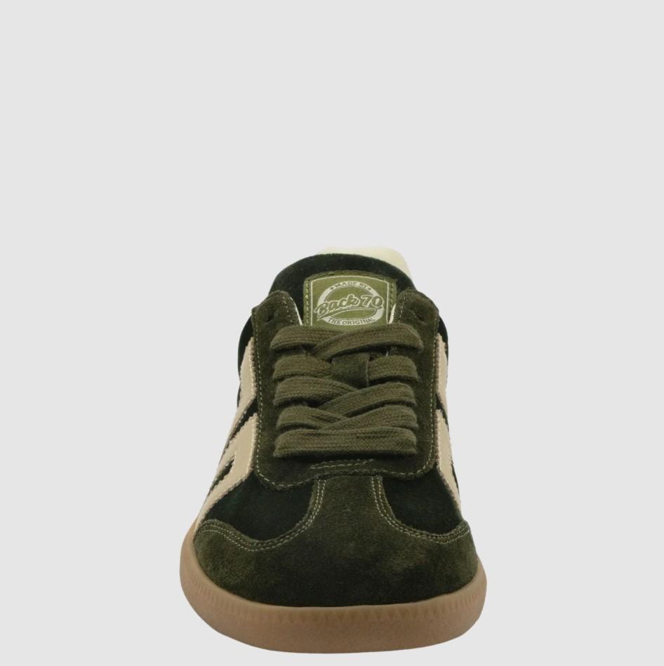 A single low-top sneaker shown from the front on a light gray background. The shoe features dark olive green suede panels, beige suede side stripes, matching olive green laces, and a tan gum sole.