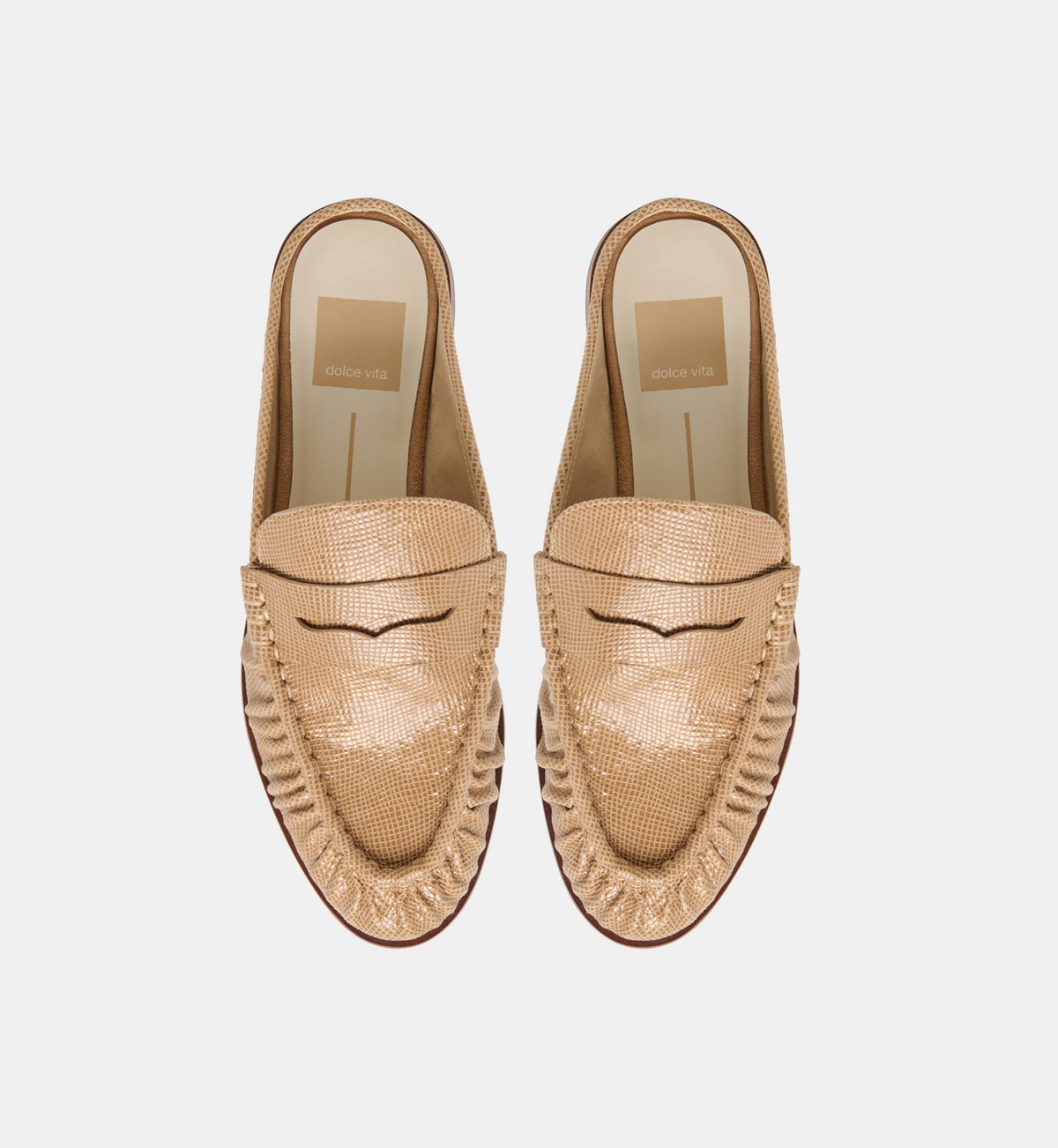 A pair of women's Dolce Vita Betzy slip-on loafers in a metallic champagne-gold textured leather, shown from a top-down view on a light gray background. The shoes feature decorative fringe detailing along the sides and a stitched eyelet design on the vamp.