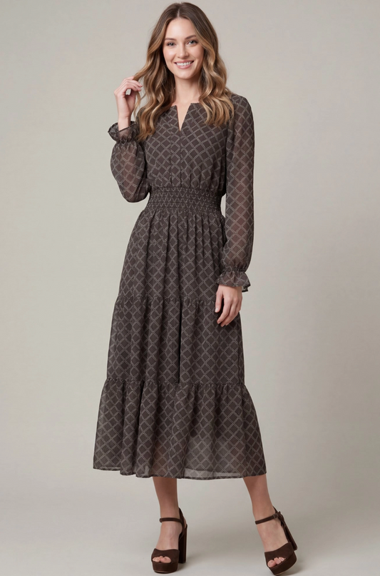 A woman modeling a long-sleeve midi dress with a brown and black geometric trellis pattern, smocked waist, and tiered ruffle hem, paired with brown platform sandals against a neutral studio background.
