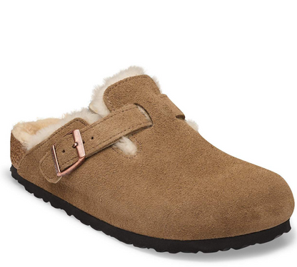 A tan suede Birkenstock clog with a soft cream shearling lining and a rose gold buckle strap, shown from a three-quarter angle on a white background.