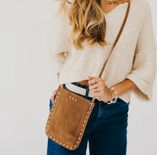 A woman carrying a brown suede crossbody bag with gold-tone studs and a strap.