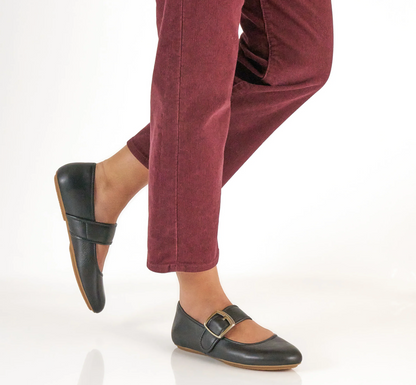 A person wearing burgundy corduroy pants and Dansko Matilda black leather Mary Jane flats with gold-tone buckle straps, shown from the knees down against a clean white studio background.