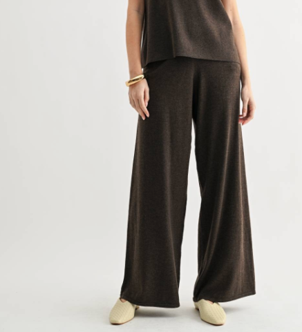 A model wearing dark brown wide-leg knit pants, a matching dark brown top, and cream-colored slip-on shoes, photographed against a light gray studio background.