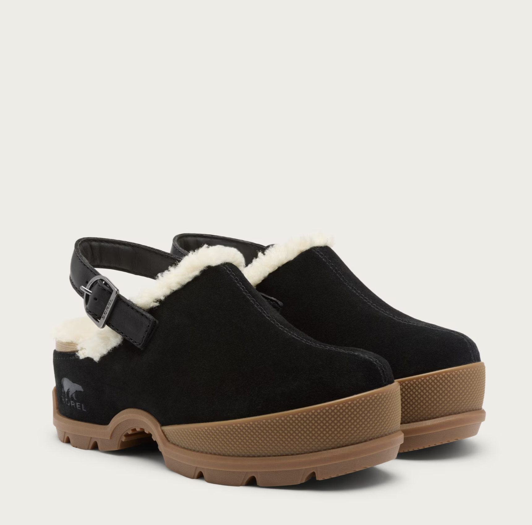 A pair of Sorel black suede clogs with white shearling lining, black ankle straps, and brown rubber soles, shown on a light beige background.