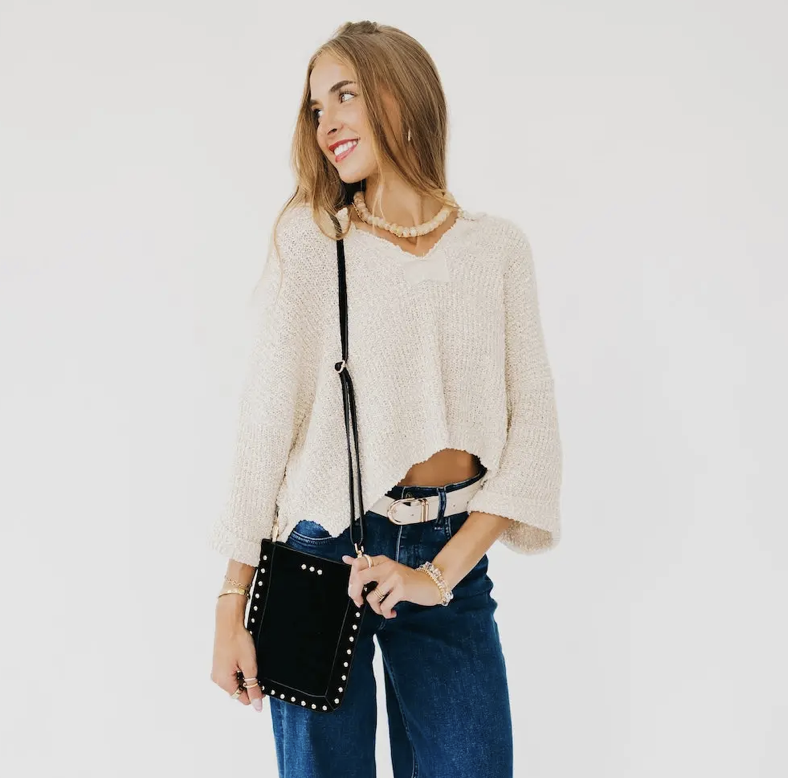 A woman with a black studded crossbody phone  bag, standing against a plain white background.