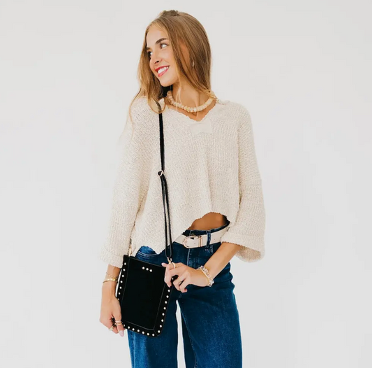 A woman with a black studded crossbody phone  bag, standing against a plain white background.