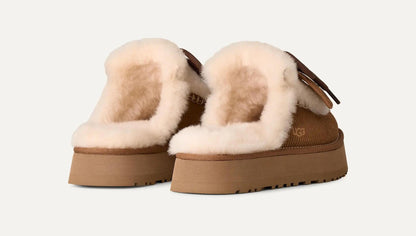 A pair of UGG platform Disquette Heritage slippers with thick tan soles and fluffy cream shearling lining, shown from a three-quarters angle on a light off-white background.