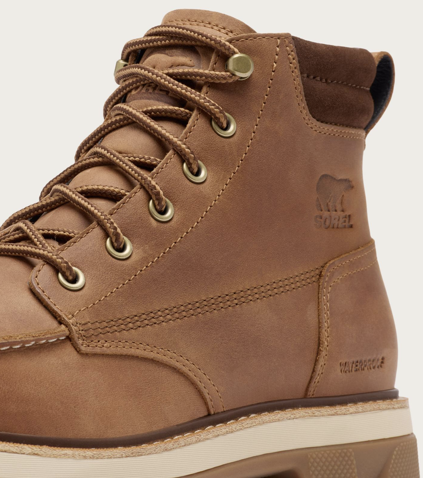 Close-up of a brown suede high-top waterproof boot with metal eyelets, brown laces, and an embossed Sorel logo on the side, shown against a light neutral background.