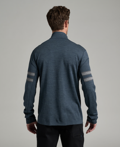 A man viewed from behind wearing a Kuhl Team heathered slate blue quarter-zip pullover with gray stripe details on the sleeves, paired with black pants, against a solid gray studio background.