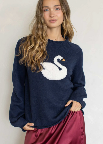 A woman wearing a navy blue knit sweater with a large white swan motif on the front, paired with a shiny burgundy skirt, against a plain light background.