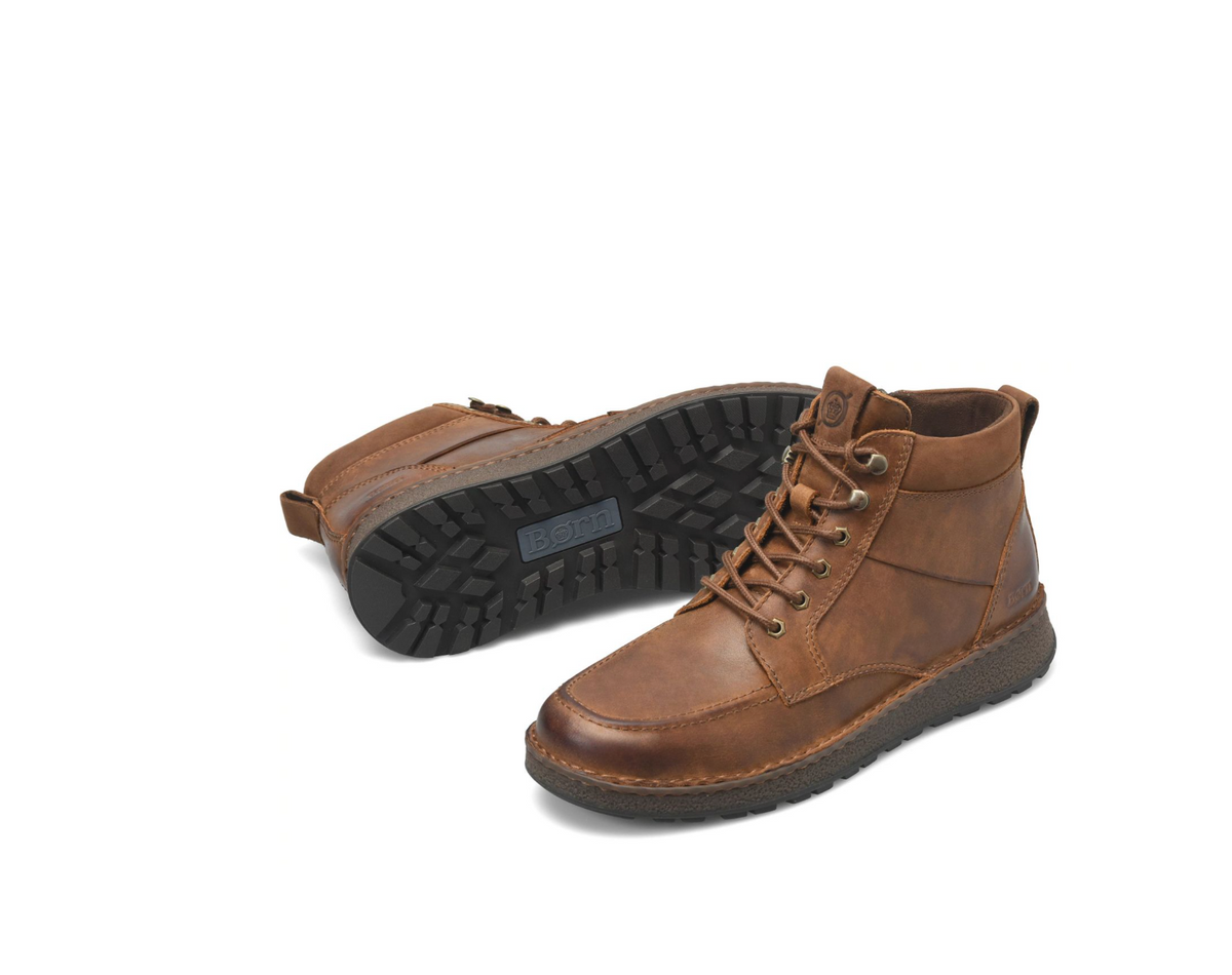 A pair of brown Børn Rex  leather lace-up ankle boots, with one boot standing upright showing the side and front, and the other lying on its side showing the black treaded outsole.