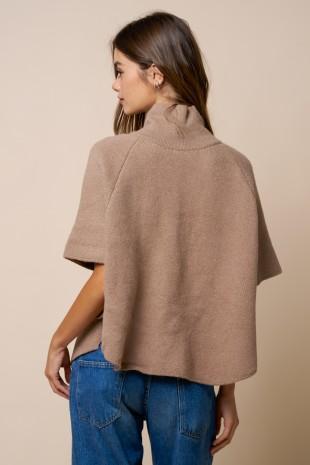 Woman wearing a beige cape over a blue outfit on a beige background