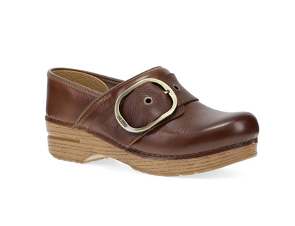 A brown leather Dansko clog shoe with a chunky wooden platform heel and a large brass buckle strap, shown from a three-quarters angle on a white background.