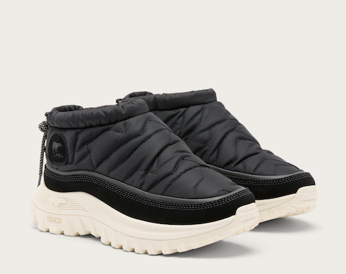 A pair of black Sorel quilted ankle-height slip-on winter boots with thick cream-colored soles, shown on a light off-white background.