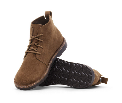 A pair of Birkenstock Uppsala Mid Boot in Dark Tea with suede upper and shearling lining lying on its side to show the textured black sole, set against a plain white background.