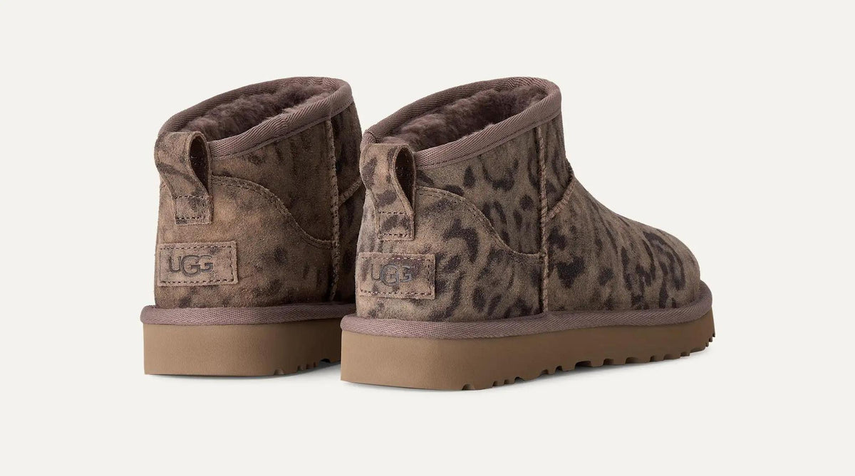 A pair of UGGClassic Ultra Mini  boots in a brown and beige leopard print pattern, shown from the back against a light off-white background.