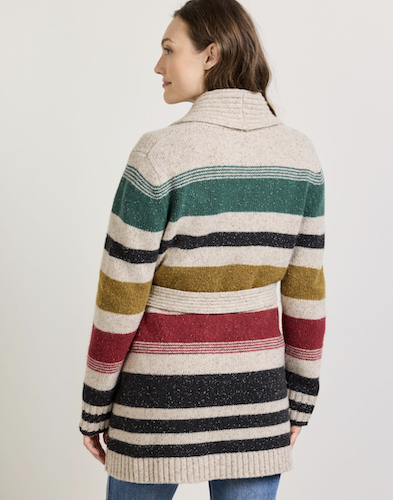 A woman shown from the back wearing a long-sleevePendleton wool-knit sweater with horizontal stripes in cream, green, black, mustard yellow, red, and navy, paired with blue jeans against a plain light gray studio background.