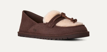 A single UGG Zora slip-on loafer in dark brown suede with a cream-colored shearling lining and a matching brown leather tassel detail, shown against a light off-white background.