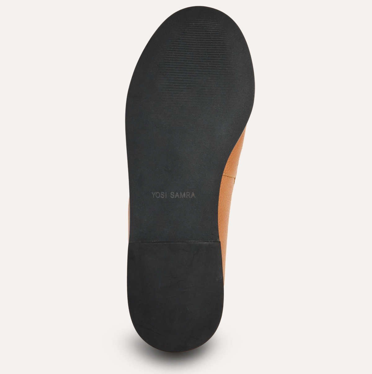 A top-down view of a shoe's sole, showing a black rubber outsole with the brand name 'YOSI SAMRA' printed in gray, alongside a tan leather side panel, on a light off-white background.