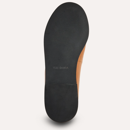 A top-down view of a shoe's sole, showing a black rubber outsole with the brand name 'YOSI SAMRA' printed in gray, alongside a tan leather side panel, on a light off-white background.