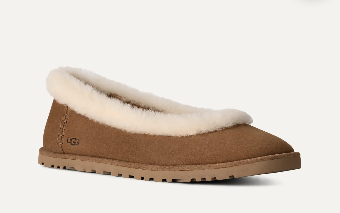 A single UGG slip-on ballet flat  in tan suede with a thick cream shearling collar and a tan rubber sole, shown from a side profile on a light off-white background.