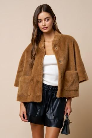 Woman wearing a brown teddy coat over a white top and black leather shorts on a beige background